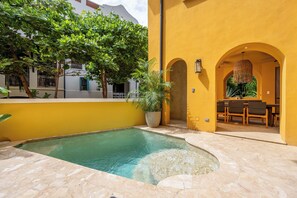 A swimming pool with a stone border, a dining area with chairs and a table, and a yellow building with an arched doorway. - Las Catalinas Luxury Villa Pool & Beach Club Access (Las Catalinas)