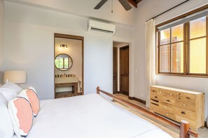 A hotel room with a bed, a vanity with a mirror, a wooden dresser, and a window with curtains. - Las Catalinas Luxury Villa Pool & Beach Club Access (Las Catalinas)