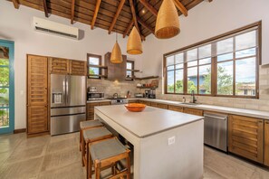 A modern kitchen with a large island, stainless steel appliances, wooden cabinets, and large windows. - Las Catalinas Luxury Villa Pool & Beach Club Access (Las Catalinas)