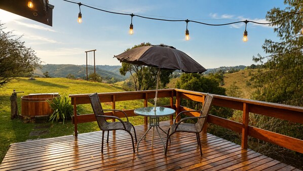 A wooden deck with a table and chairs, surrounded by a railing, overlooking a hilly landscape.