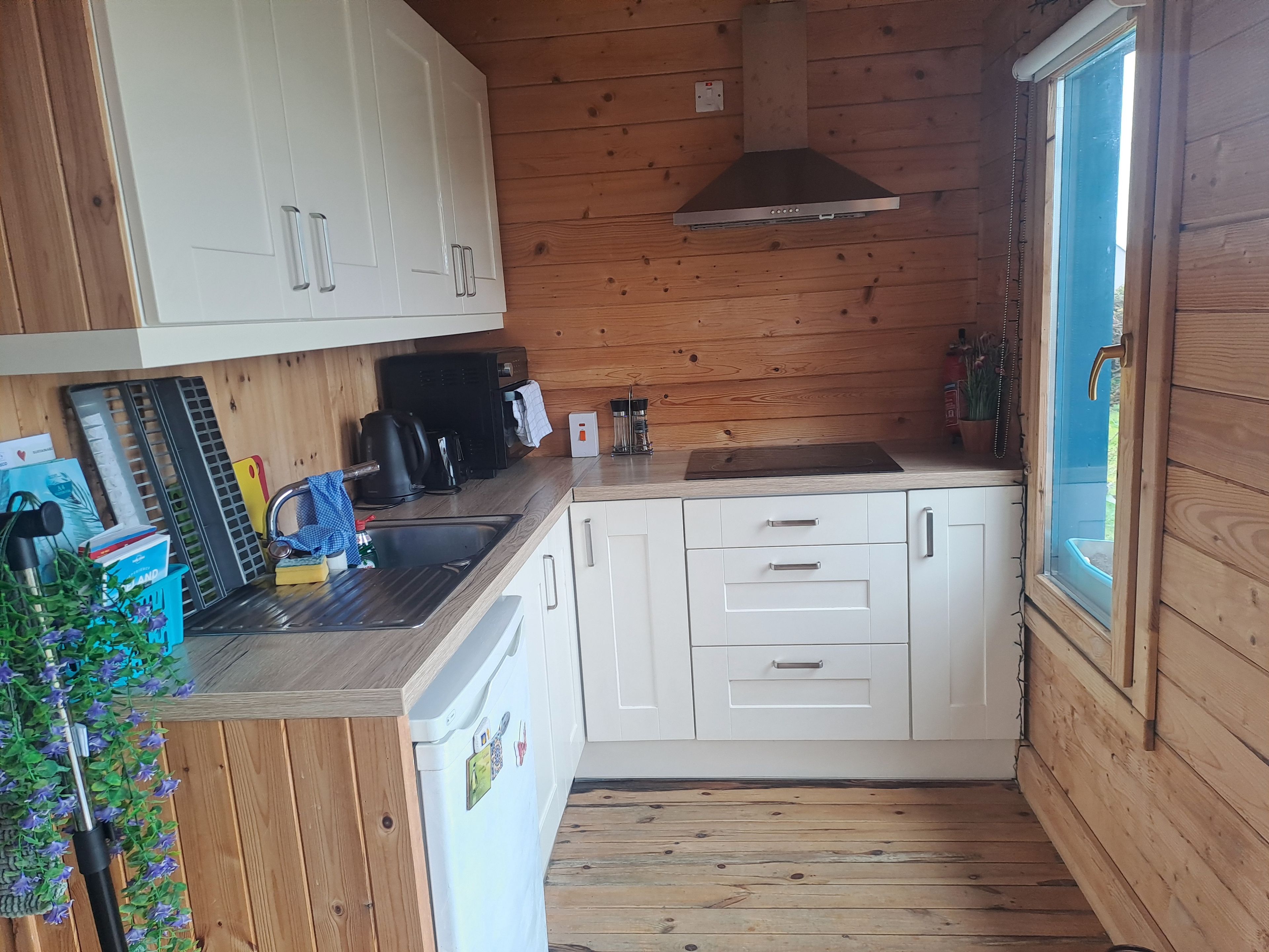 A compact kitchen with wooden walls, white cabinets, a stainless steel sink, and a built-in range hood.