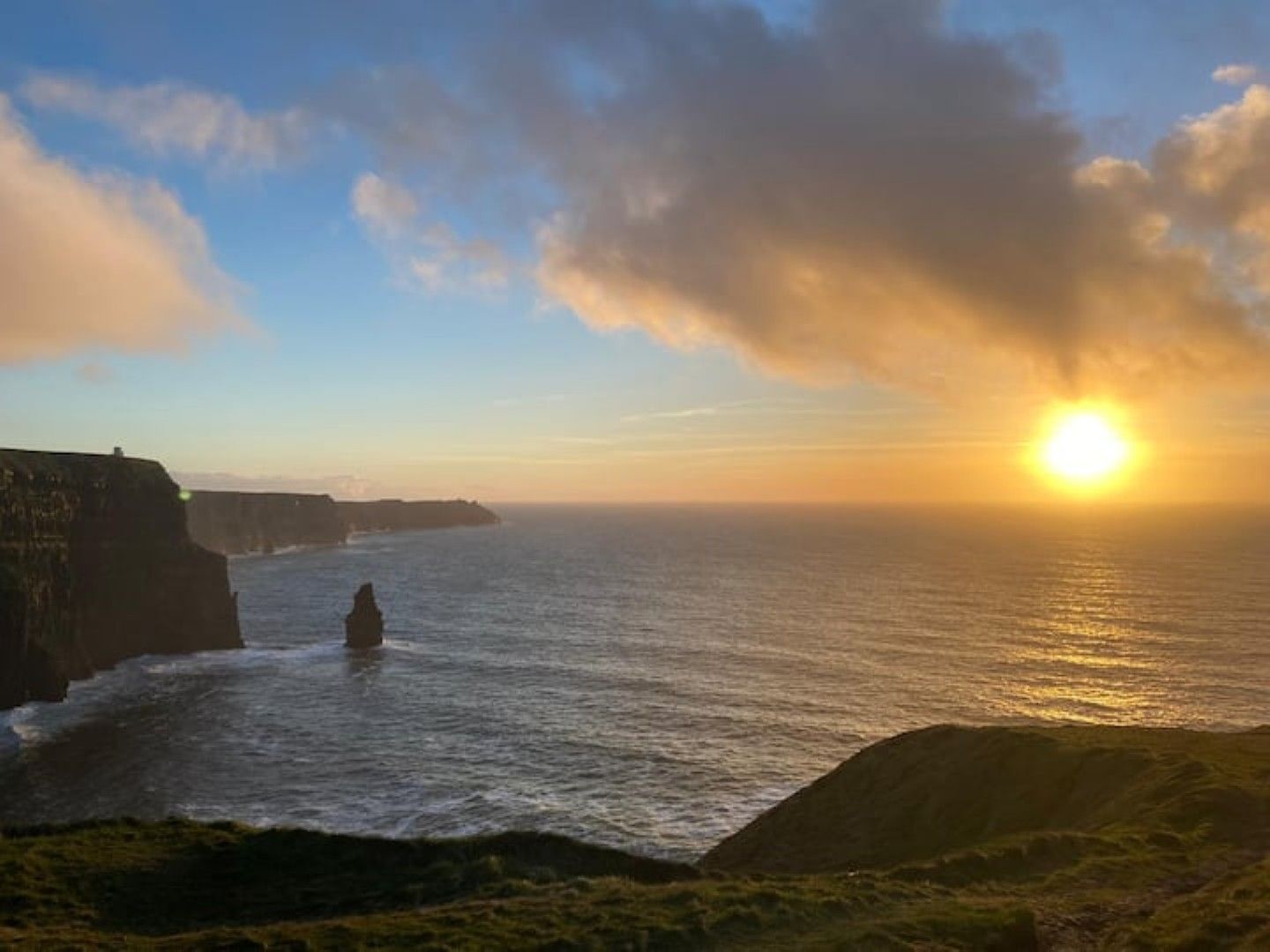 A coastal landscape with a cliff and ocean during sunset.