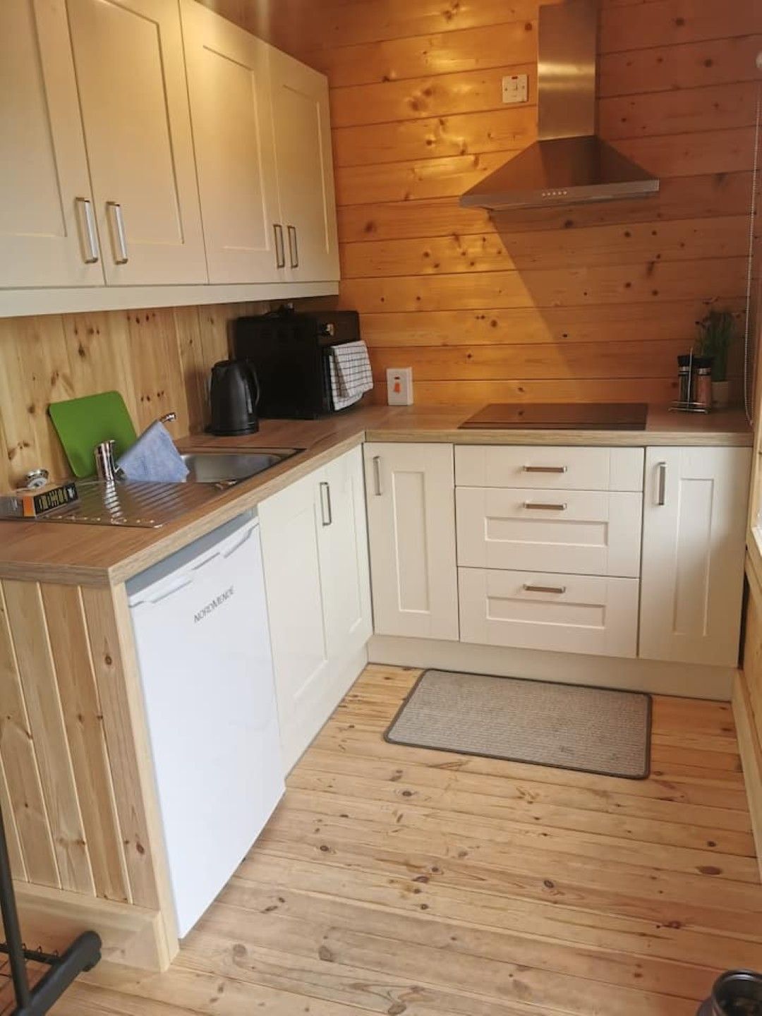 Cocina compacta con paredes y armarios de madera, lavavajillas integrado y extractor de acero inoxidable.
