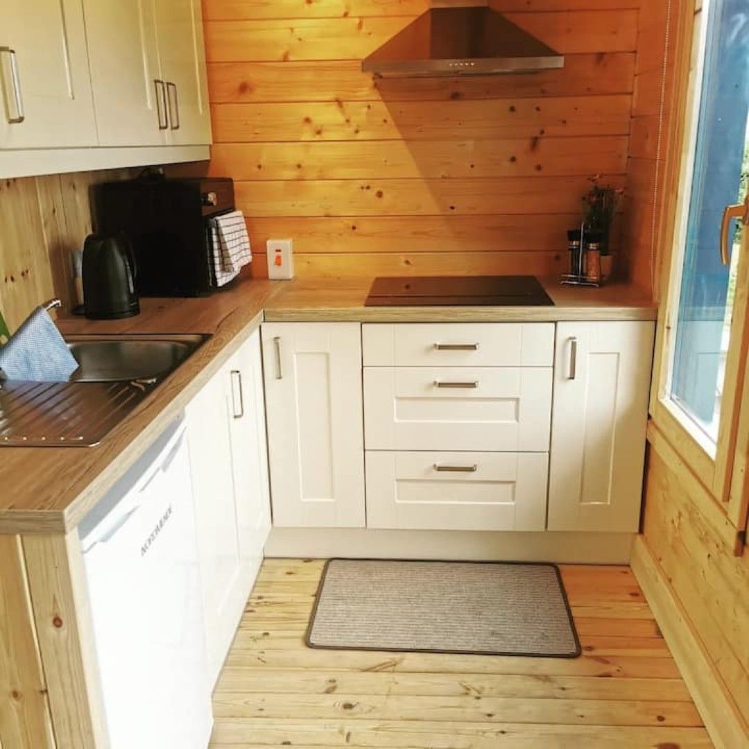 Cocina compacta con paredes de madera, un lavamanos de acero inoxidable y armarios blancos.