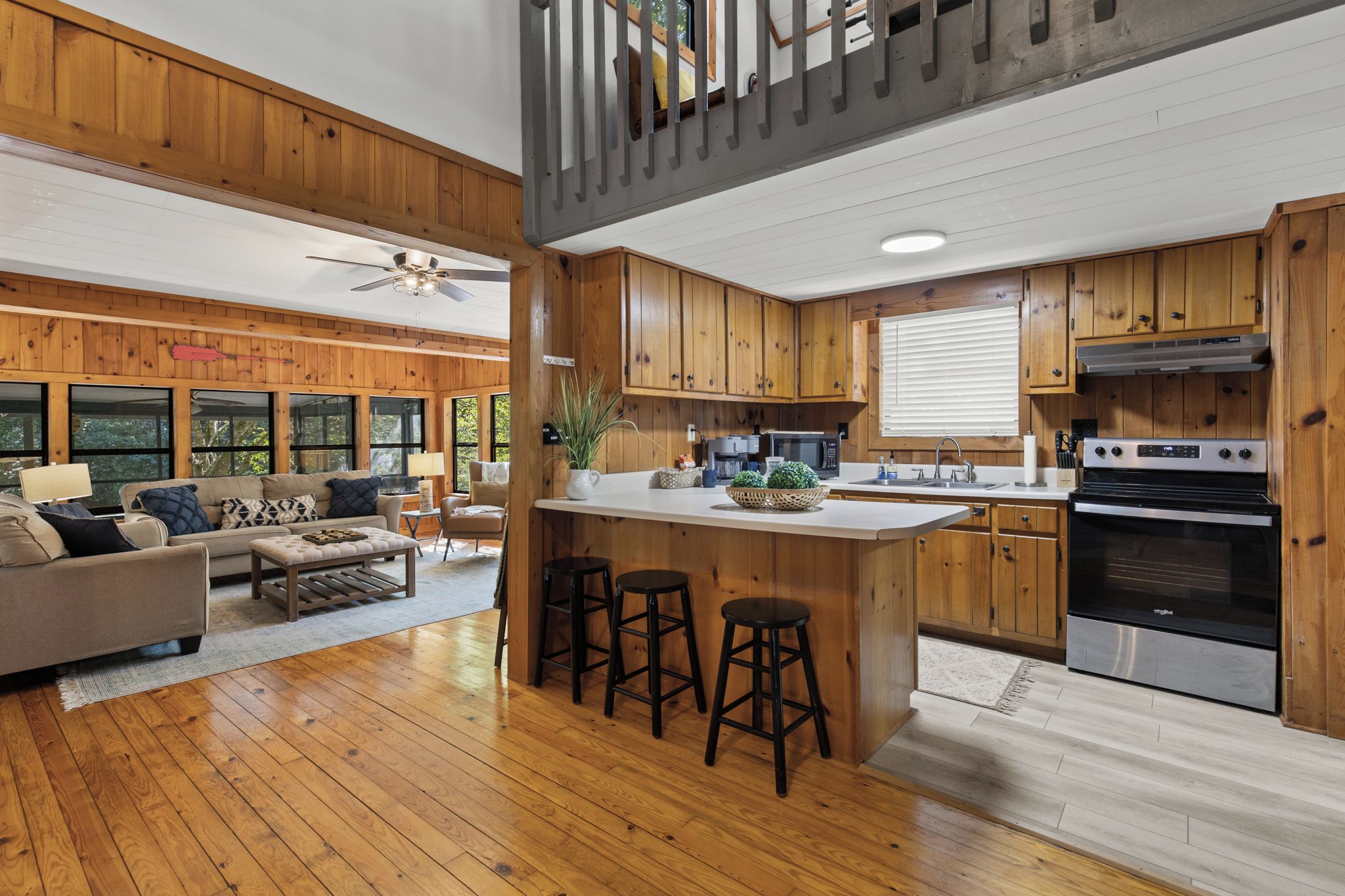 A spacious living area with a wooden floor, a sofa, and a dining area with stools.