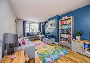 A modern living room with a sofa, a coffee table, a bookshelf, and a colorful rug. - Spacious Family Home In Southsea - Pass The Keys (Portsmouth)