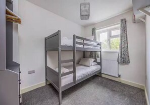 Uma cama de solteiro em um quarto com radiador, janela com cortinas e guarda-roupa.