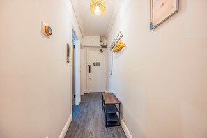 Un couloir avec un plancher en bois, une petite table, une porte et un luminaire fixé au mur.