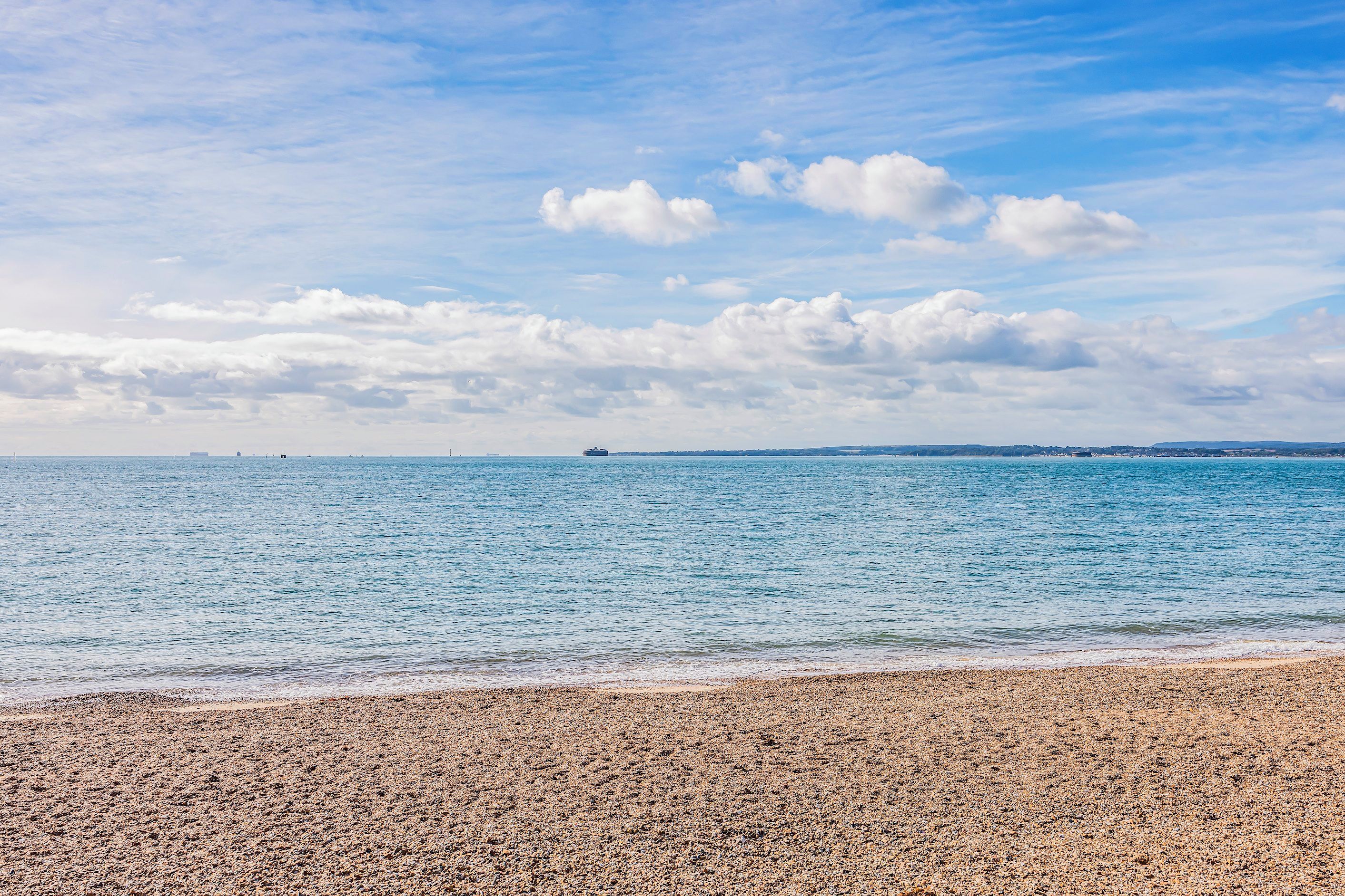 Une plage de galets, une mer calme et un navire au loin.