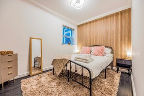 A bedroom with a bed, a dresser, a mirror, a window, and a wooden wall panel. - Basement Flat Minutes From Pier And Beach - Pass the Keys (Portsmouth)