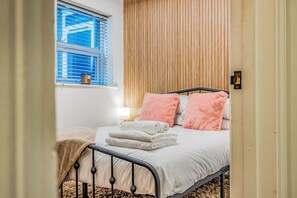 A bedroom with a bed, pillows, a window, and a wooden wall. - Basement Flat Minutes From Pier And Beach - Pass the Keys (Portsmouth)