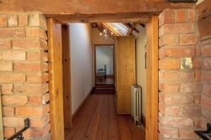 A narrow hallway with wooden beams and brick walls, leading to a room with a bed and a radiator. - The Threshing Barn - Pass the Keys (Blankney Fen)