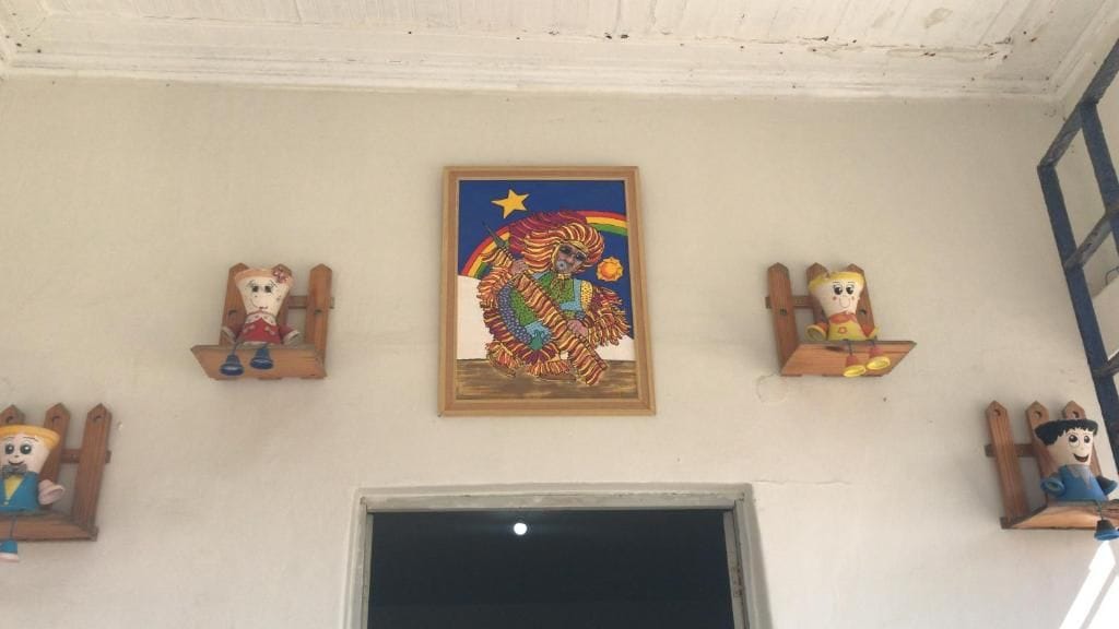 Una habitación con un ventanal amplio, un cuadro enmarcado y tres estanterías de madera con figuritas.
