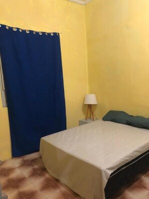 A room with a bed, a nightstand, a lamp, and a blue curtain.