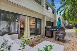 A patio area with a grill, outdoor seating, and a sliding glass door leading to a living space. - Islamorada Townhouse - Sunsets, Beach & Sparkling Pool! (Islamorada)