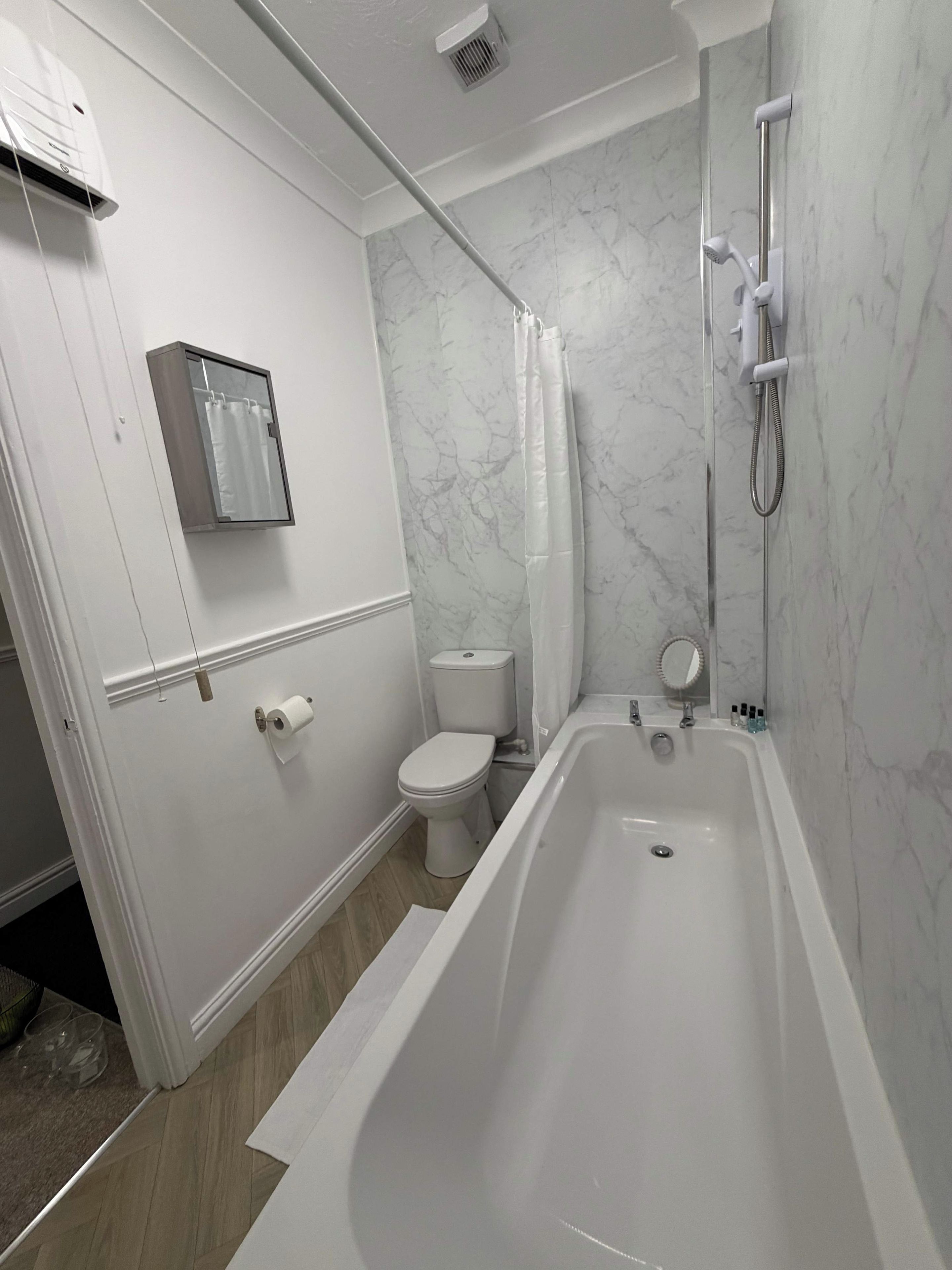 Et badeværelse med badekar, toilet og bruseniche.