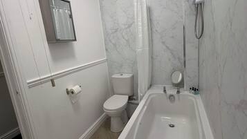 Et badeværelse med badekar, toilet og bruseniche.