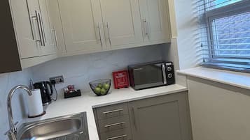Een moderne keuken met een ingebouwde magnetron, een waterkoker en een schaal fruit op het aanrecht.