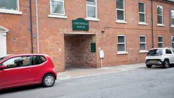 A red car parked in front of a brick building with a sign reading 'Larchfield House'.