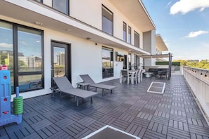 Une terrasse extérieure moderne dotée d’un espace repas, de chaises longues et offrant une vue sur la ville.