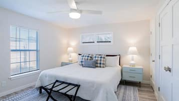 A bedroom with a bed, two bedside tables, a ceiling fan, and a window with blinds.