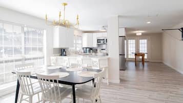 A modern kitchen with white cabinets, a dining area with a black table and white chairs, and a chandelier.