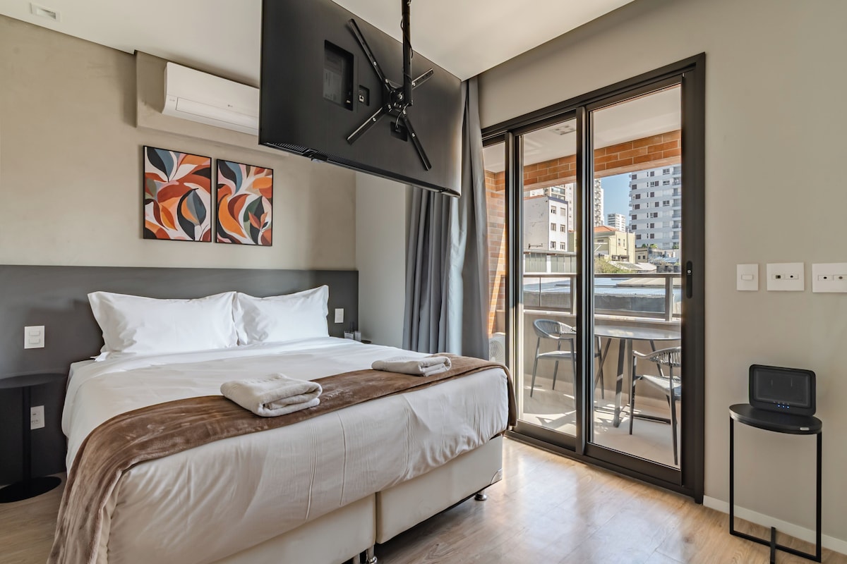 Een hotelkamer met een bed, een televisie, een balkon met een tafel en stoelen, en kunst aan de muur.