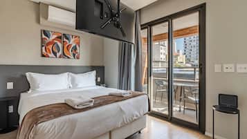 Een hotelkamer met een bed, een televisie, een balkon met een tafel en stoelen, en kunst aan de muur.