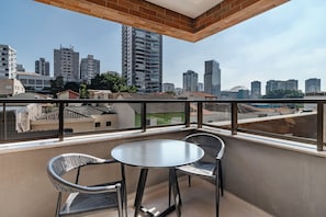 A balcony with a round table and two chairs, overlooking a cityscape with various buildings. - Vom by Bhomy (São Paulo)