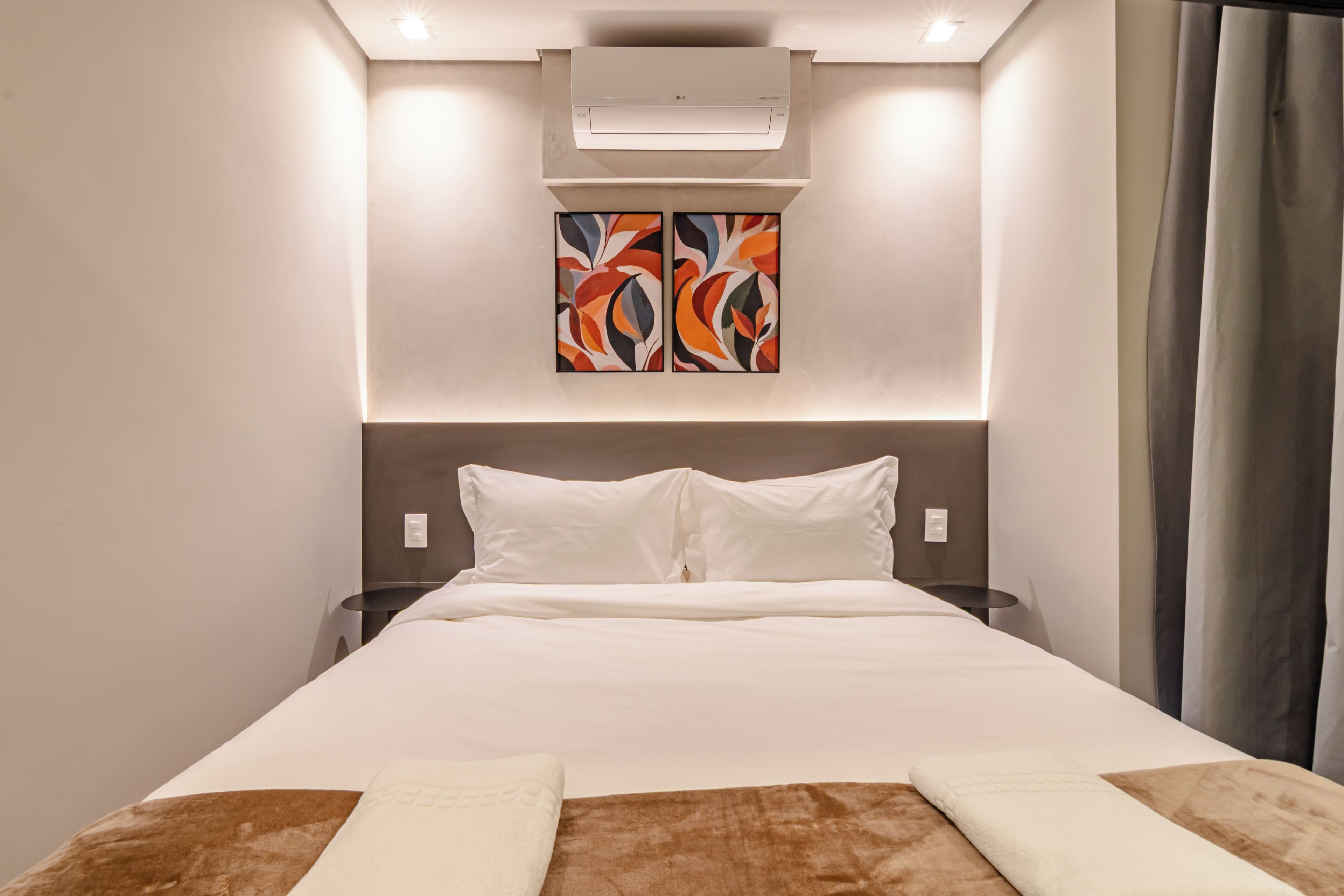 Een hotelkamer met een bed, een wandairconditioner en een schilderij boven het bed.