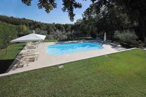 Una piscina rectangular con un borde de baldosas, rodeada por un césped y árboles.