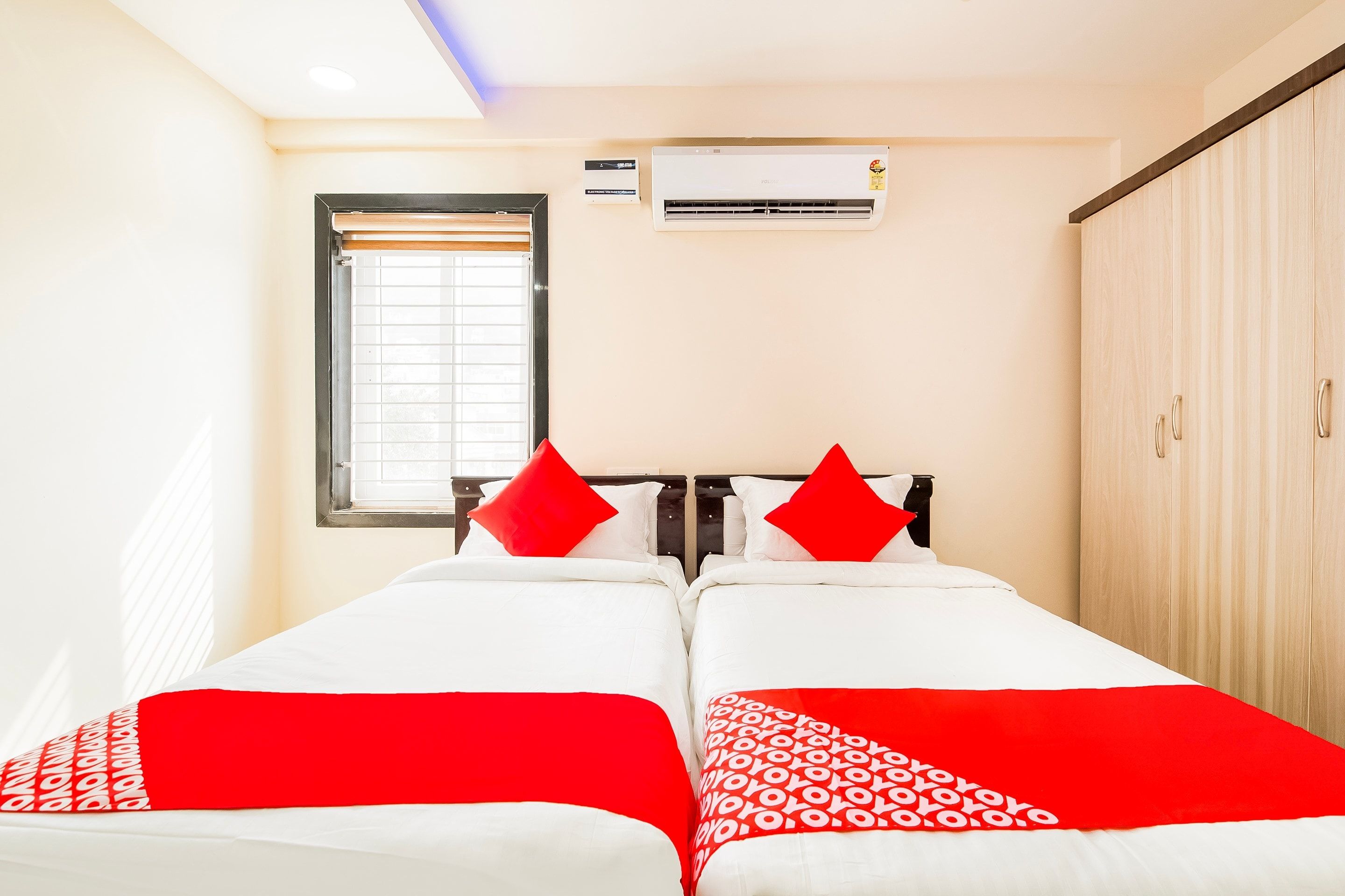 Habitación de hotel con dos camas, una ventana con persianas, un equipo de aire acondicionado y un armario.