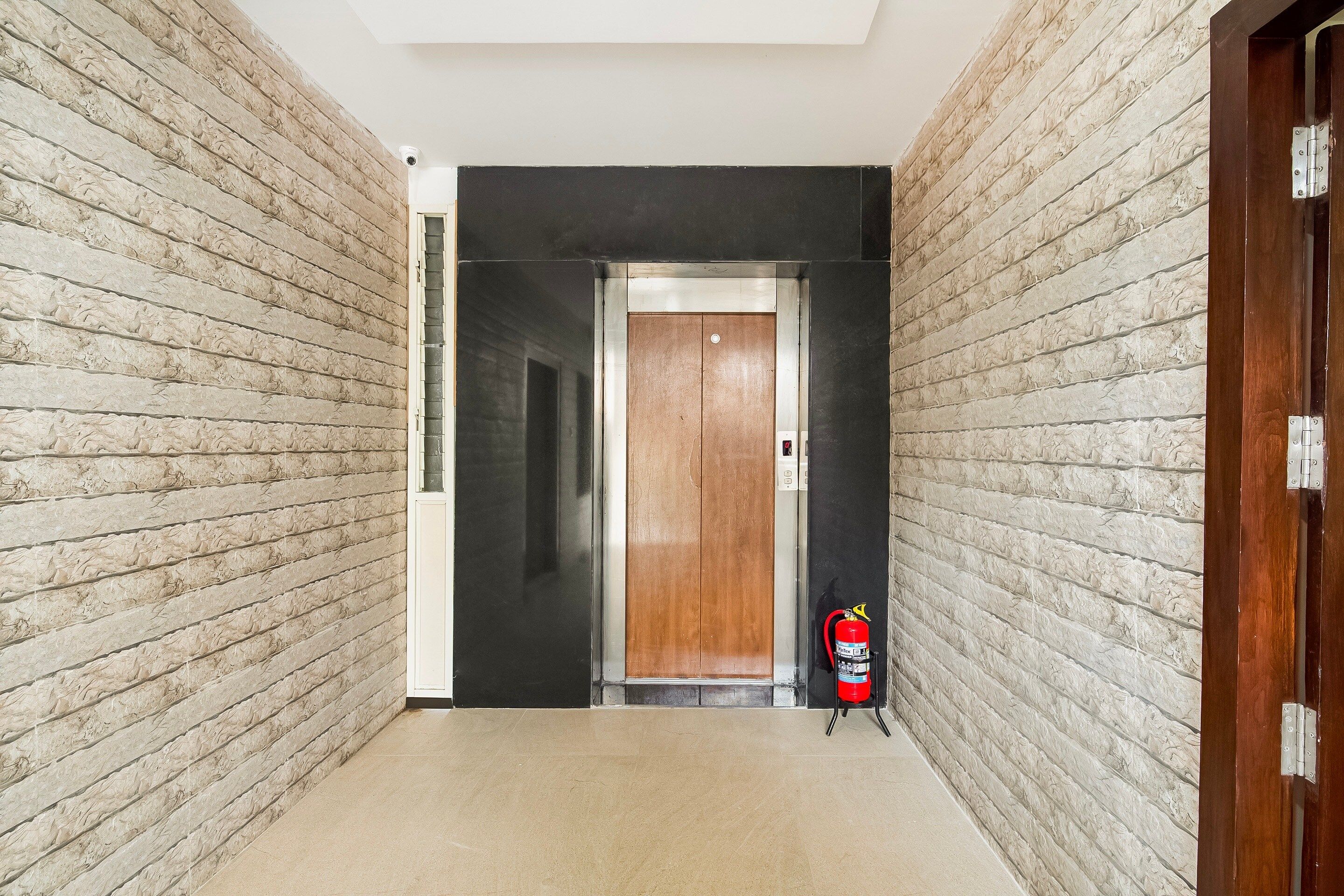 Un pasillo con una puerta de madera, un extintor y una cámara de seguridad instalada en el techo.