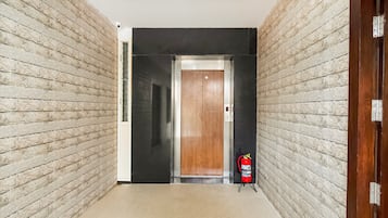 A hallway with a wooden door, a fire extinguisher, and a ceiling-mounted security camera.
