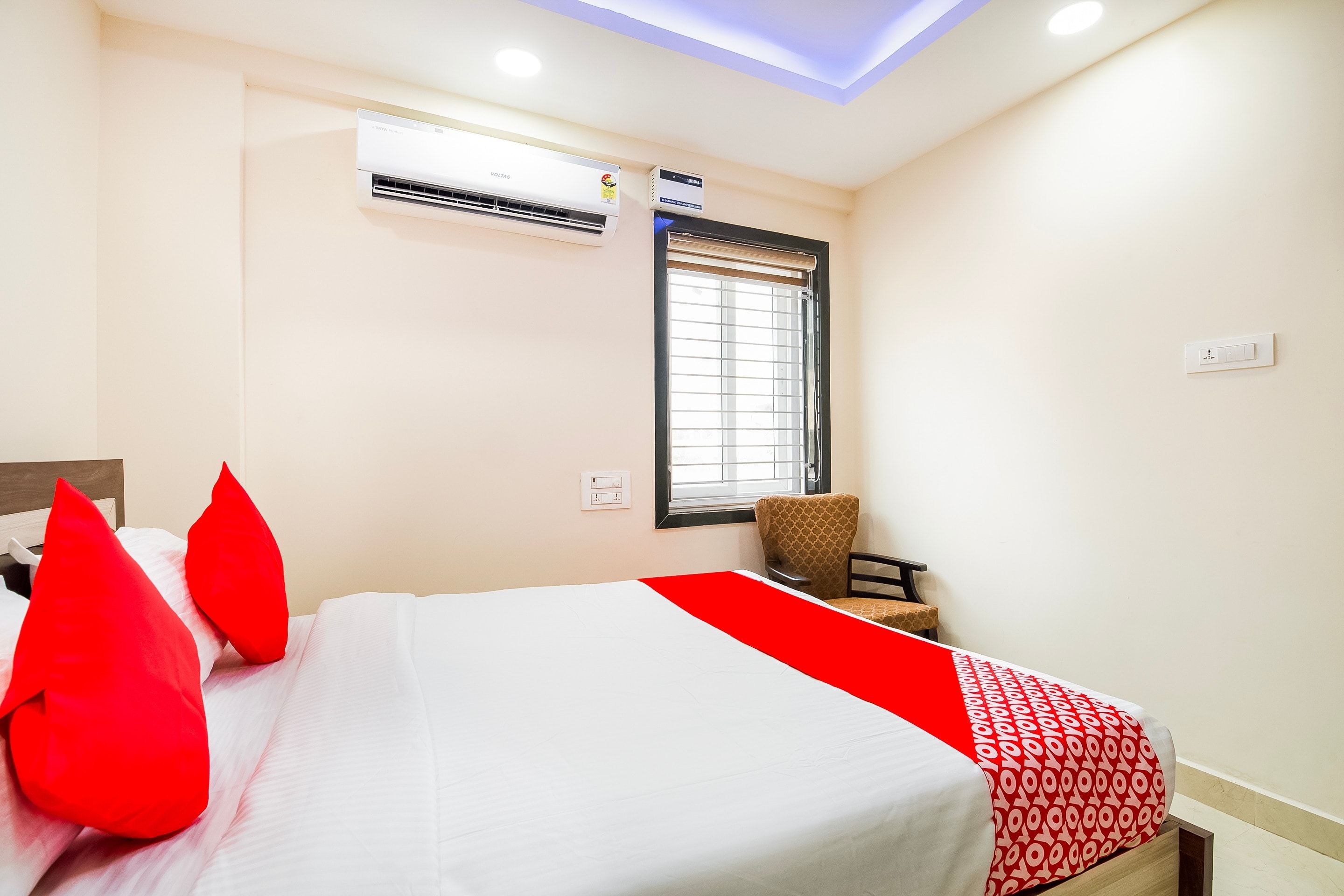 Habitación de hotel con cama, ventana con persianas, unidad de aire acondicionado y una silla.