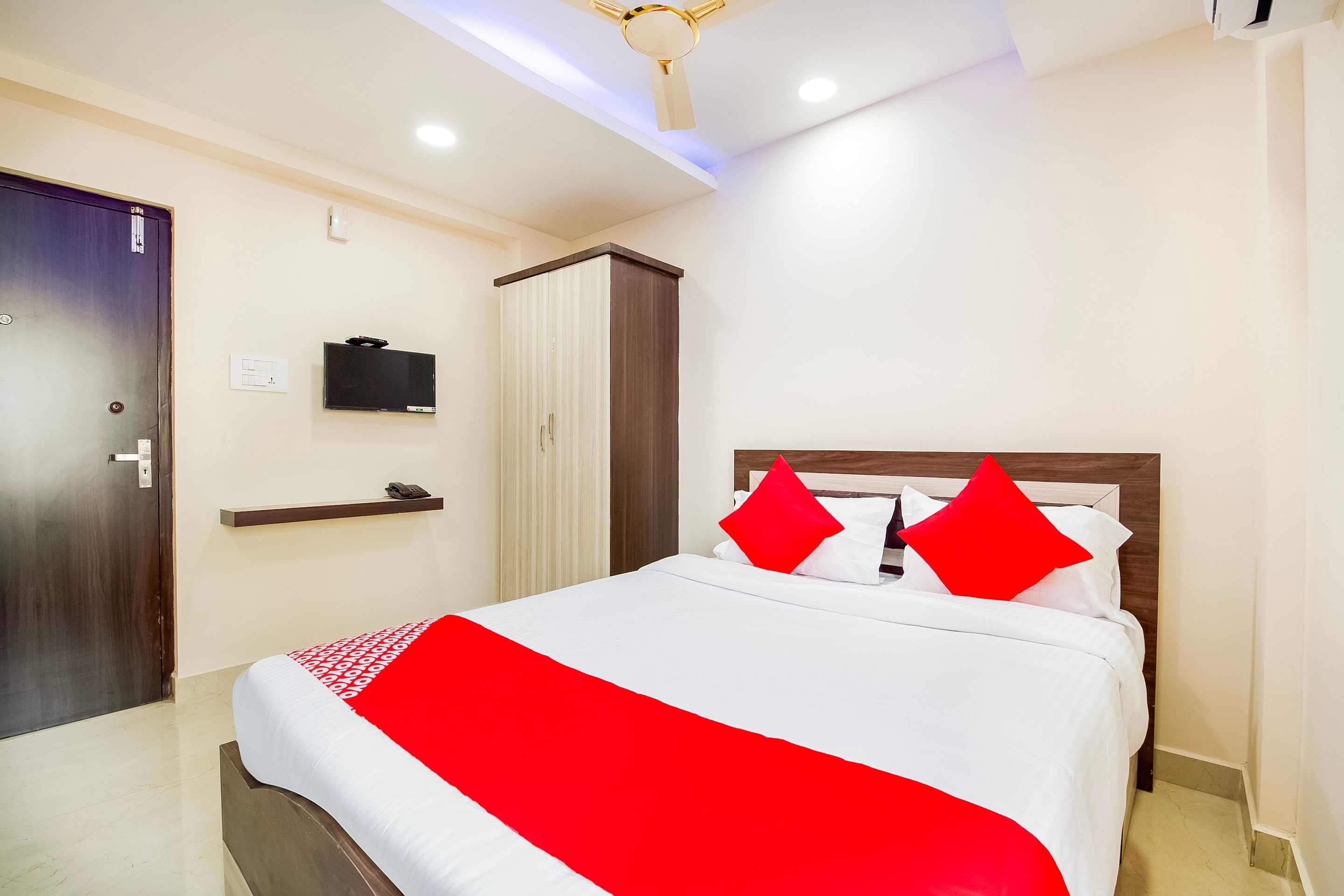 A hotel room with a bed, a television, a wardrobe, and a ceiling fan.