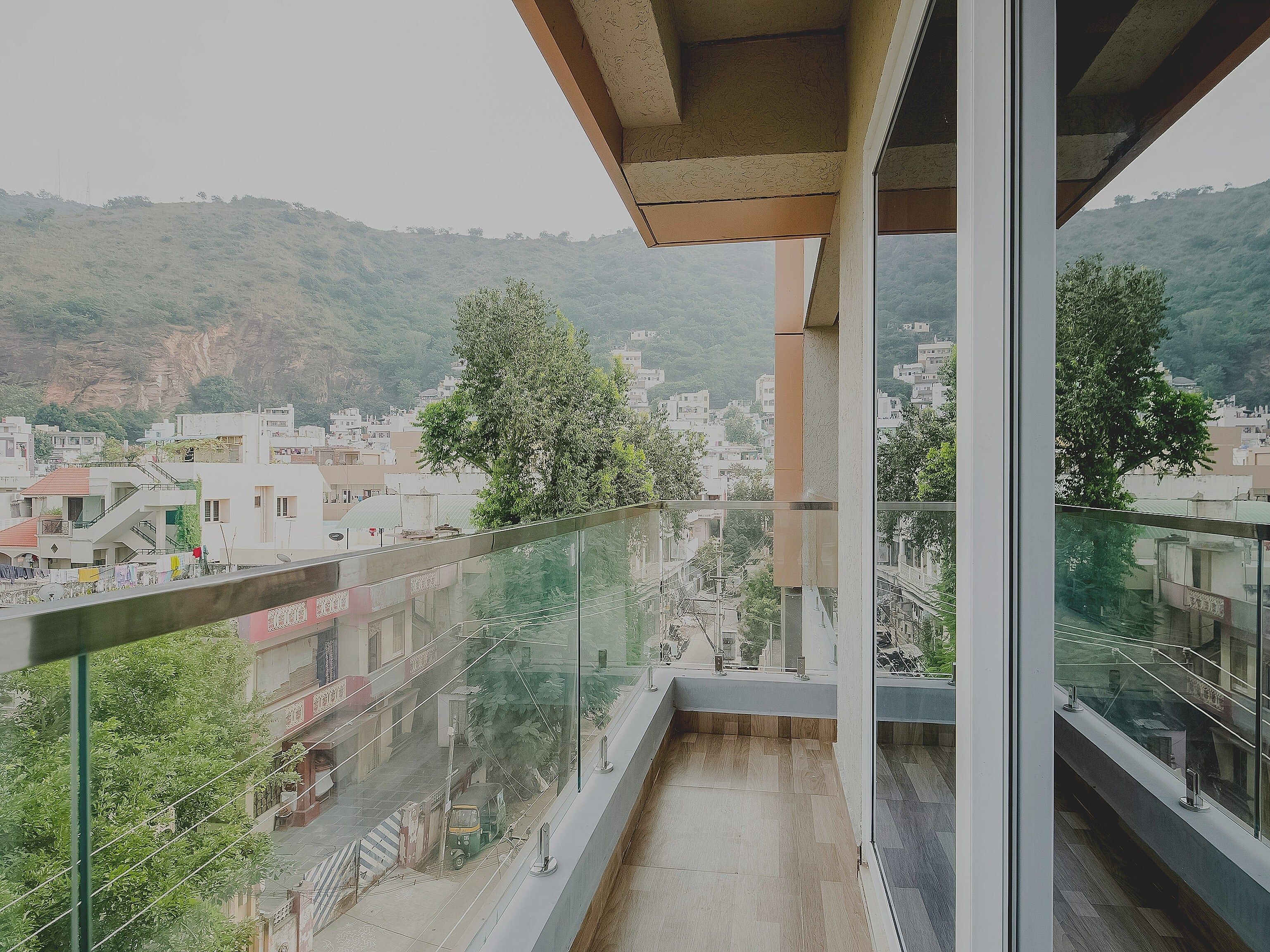 A balcony with a glass railing overlooking a residential area with trees and buildings.