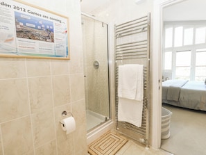 Un baño con cabina de ducha de vidrio, un perchero para toallas y un dispensador de papel higiénico.