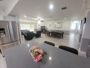 Eine moderne Küche mit integriertem Kühlschrank, ein Essbereich mit Tisch und Stühlen sowie ein Wohnzimmer mit Sofa und Flachbildfernseher.