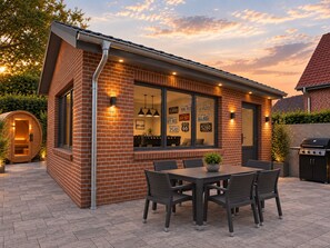 A brick house with a patio, a wooden sauna, and a barbecue grill. - Schmiede II - Vacation Home for 8 People, 4 Bedrooms & Garden (Dagebüll)