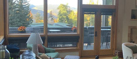 A living room with a leather sofa, a coffee table, and a view of a mountain landscape through large windows.
