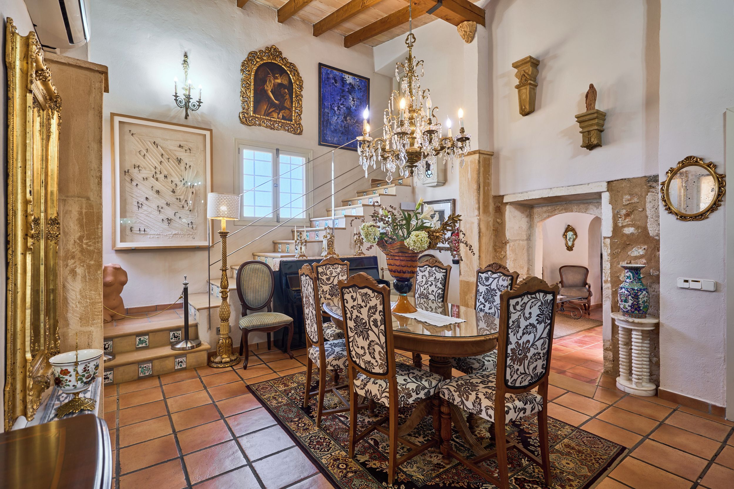 Un espace repas agrémenté d’un lustre, de fauteuils décoratifs, d’un escalier et d’une cheminée.