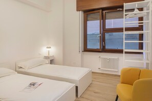Une chambre avec deux lits, une table de chevet avec une lampe, une fenêtre donnant sur un paysage agréable, un radiateur et une chaise jaune.