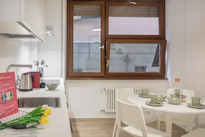 Une cuisine moderne avec une fenêtre, des armoires blanches et un coin repas comprenant une table et des chaises.