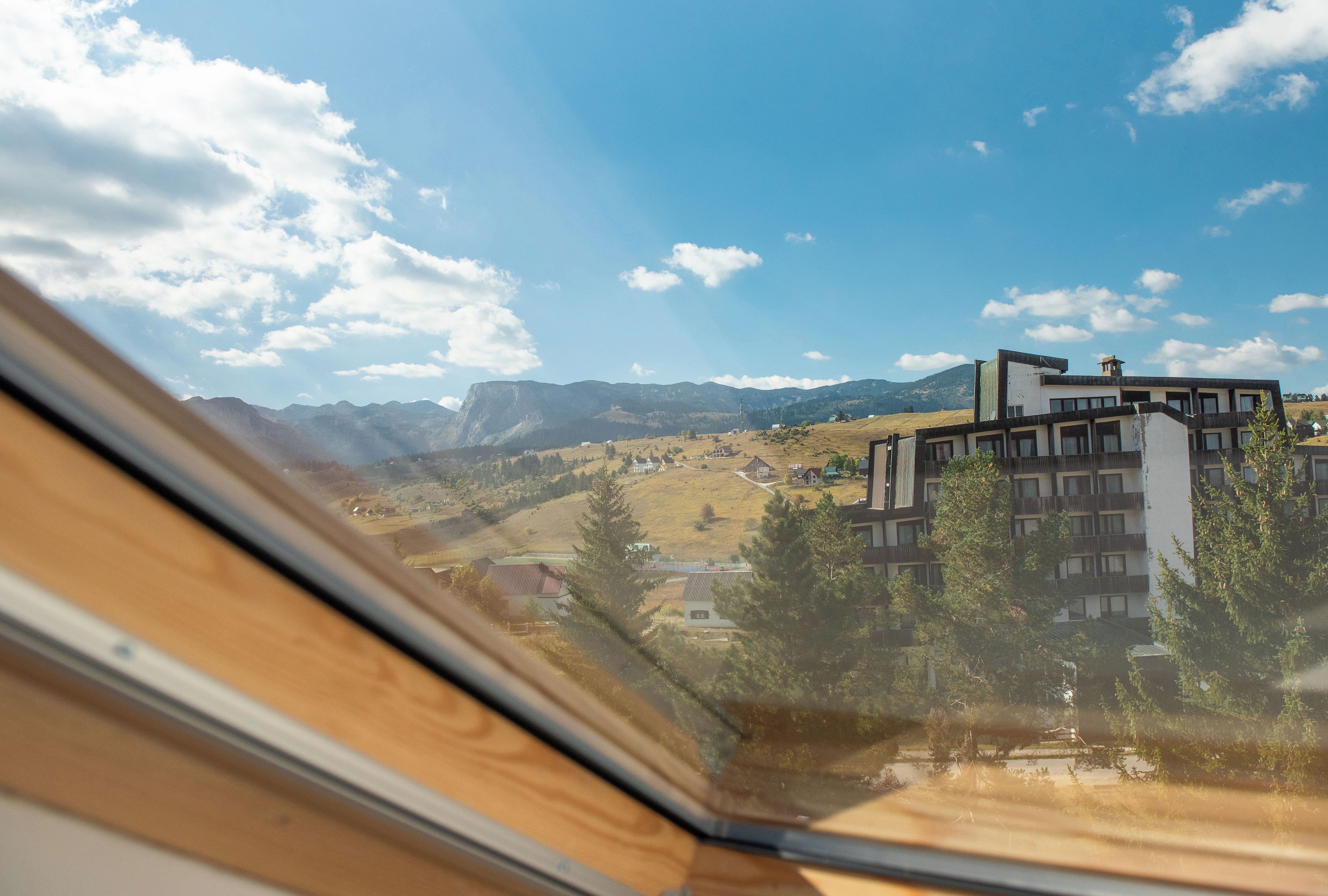 A view from inside a building looking out at a mountain range, a modern building with a flat roof, and a clear sky.