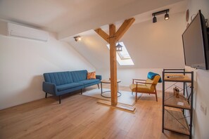 Un espace de vie de style loft avec un canapé bleu, une chaise en bois, une petite table ronde et un téléviseur fixé au mur.