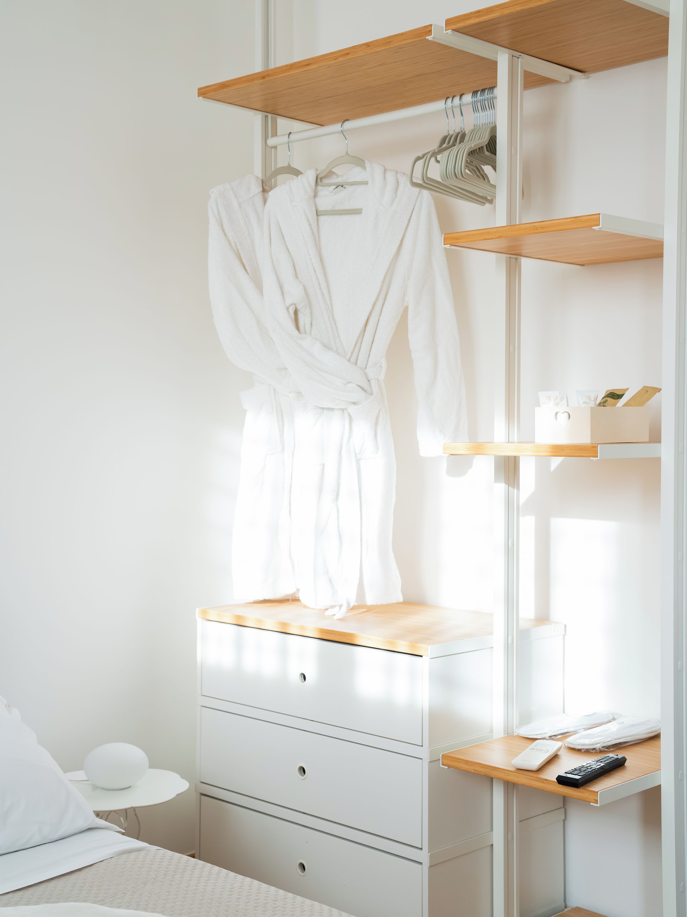 Una camera da letto con un letto, un comodino con una lampada, una cassettiera e una mensola in legno con un accappatoio.