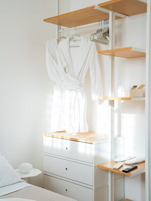 Una camera da letto con un letto, un comodino con una lampada, una cassettiera e una mensola in legno con un accappatoio.