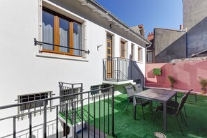 Edifici residencial amb un balcó, una taula, caires i una petita zona de jardí amb gespa artificial.