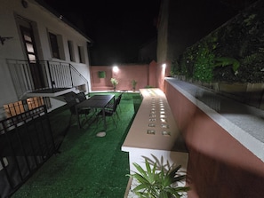 Ein möblierter Außenbereich mit Tisch und Stühlen, ein kleiner Garten und eine Mauer mit Blumenkästen.